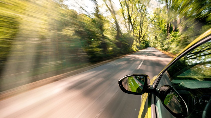 Closeup of a driver's side car mirror driving down a forest back road.