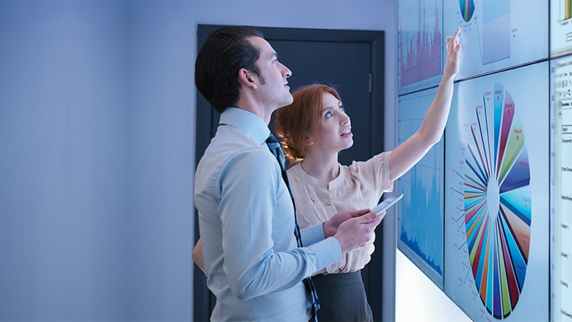 A man and a woman review Opcenter operations analytics displayed on wall monitors