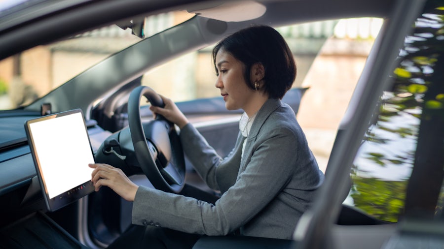 Eine Fahrerin in einem intelligenten Auto bedient den Bildschirm für Navigation und Klimaanlage, ehe sie aus der Parklücke fährt.