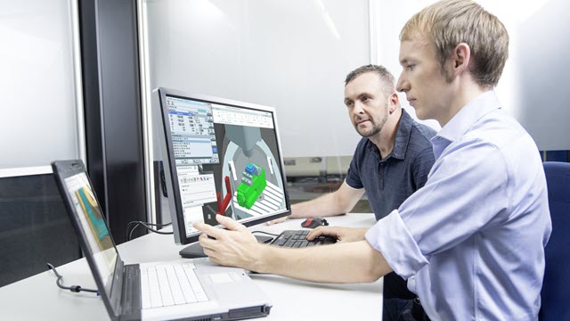 Two engineers on desk with a design shown on laptop and monitor 