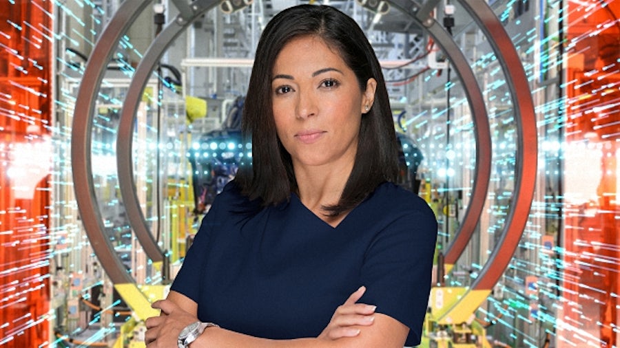 A business executive with arms crossed stands in front of the interior of an industrial parts machine shop.