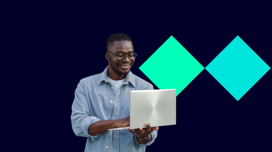 A man stands holding a laptop featuring a green diamond design on behind the screen.