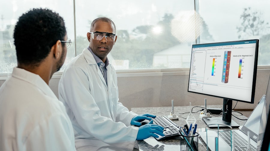 Two scientists wearing lab coats looking at each other in front of a computer screen.