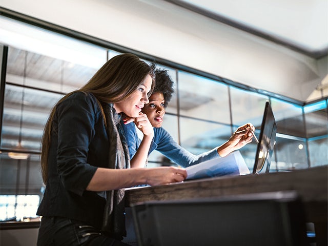 Two ladies working on their laptop in a workspace where they are discussing what they see on the laptop.