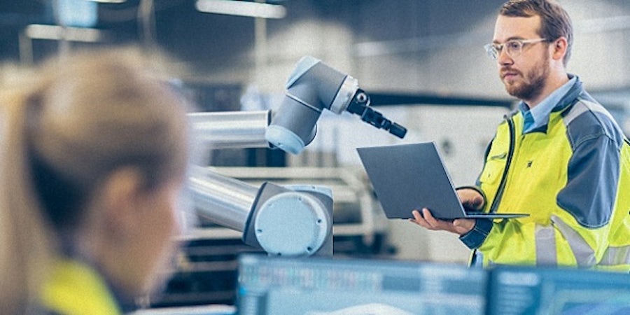 Two engineers use industrial simulation software on their computers to test an industrial robotic arm. 