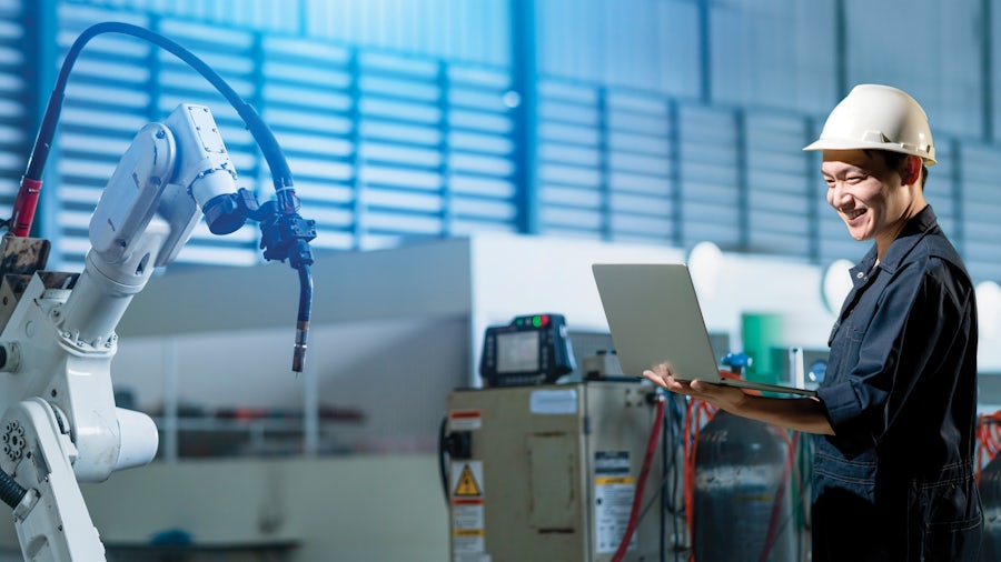 An engineer uses closed-loop manufacturing solutions on his laptop while working with an industrial robot.