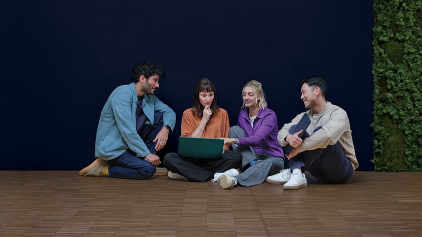 Four students sitting on the floor looking at a laptop together