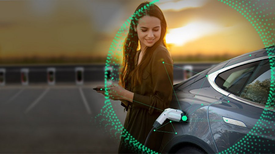 Woman on her phone standing next to an electric vehicle that is fast charging in a parking lot