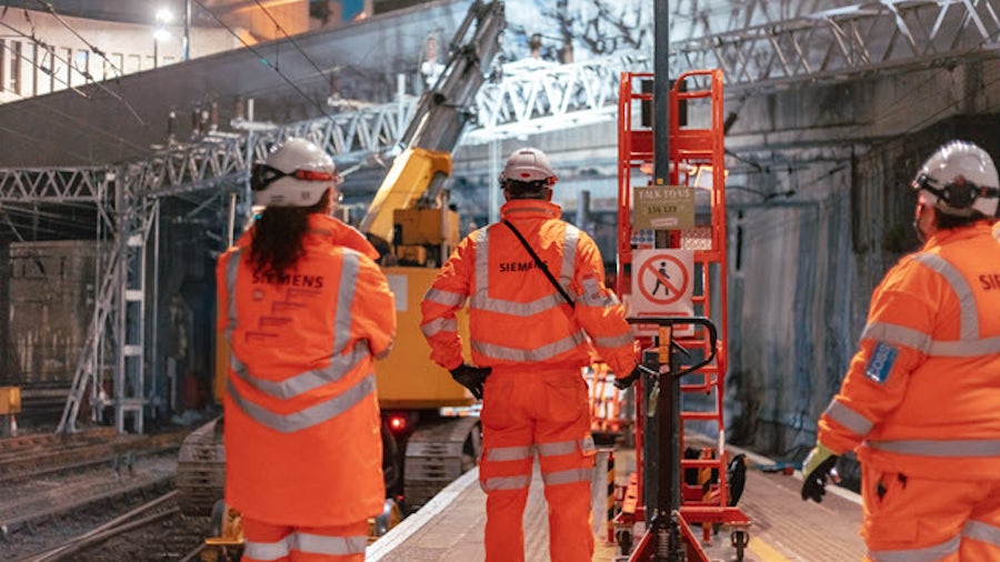 Employees in orange coats watching machine