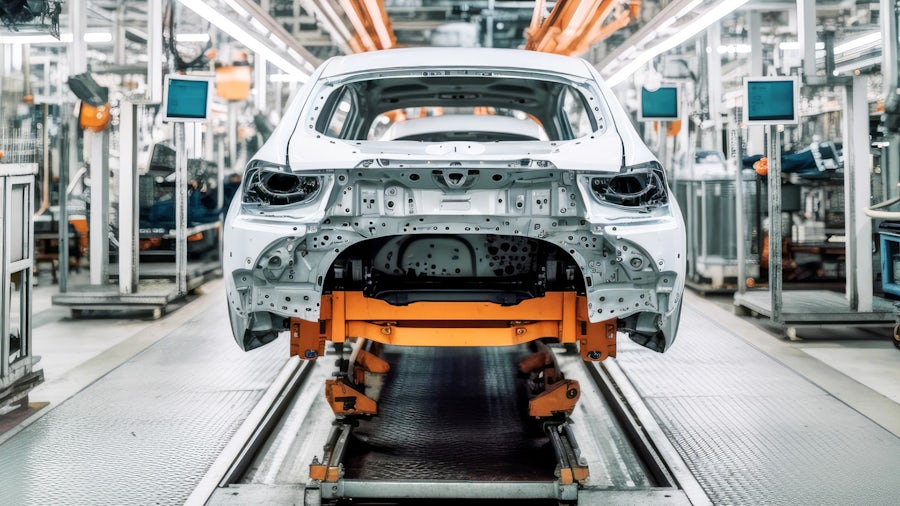 White automobile chassis on a lift in a manufacturing facility.