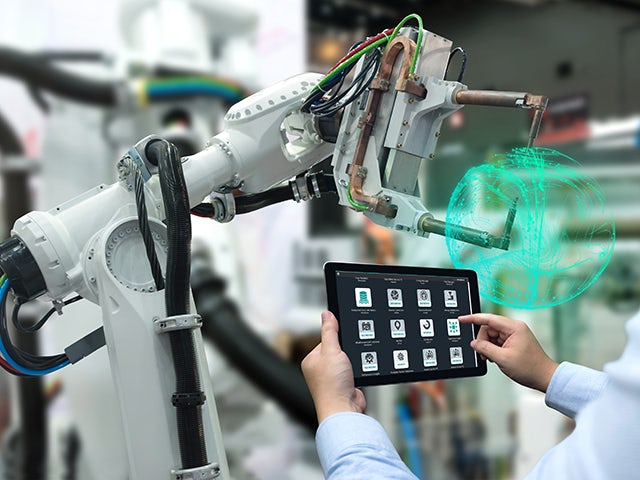 A person is holding a tablet up to a robotic arm to analyze its performance.