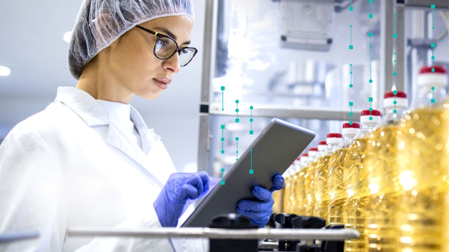 Female food and beverage manufacturing worker using a tablet on a production line with oil bottles, analyzing real-time data for process improvement and production traceability.
