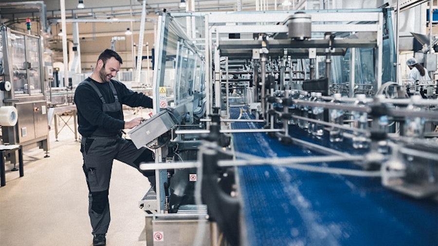 Un uomo al lavoro accanto a un macchinario industriale per l'imbottigliamento dell'acqua.