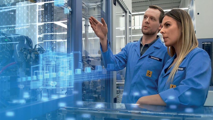 Male and female shop floor engineers reviewing electronics manufacturing operations performance with digital process overlay