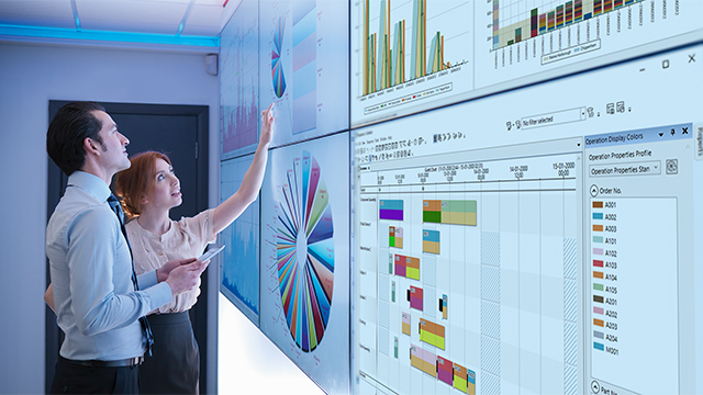 A man and a woman review Opcenter operations analytics displayed on wall monitors