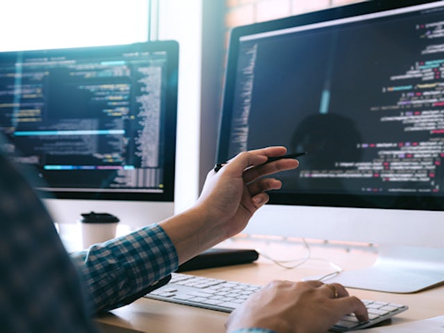 Engineer examines software C-code on dual monitors.