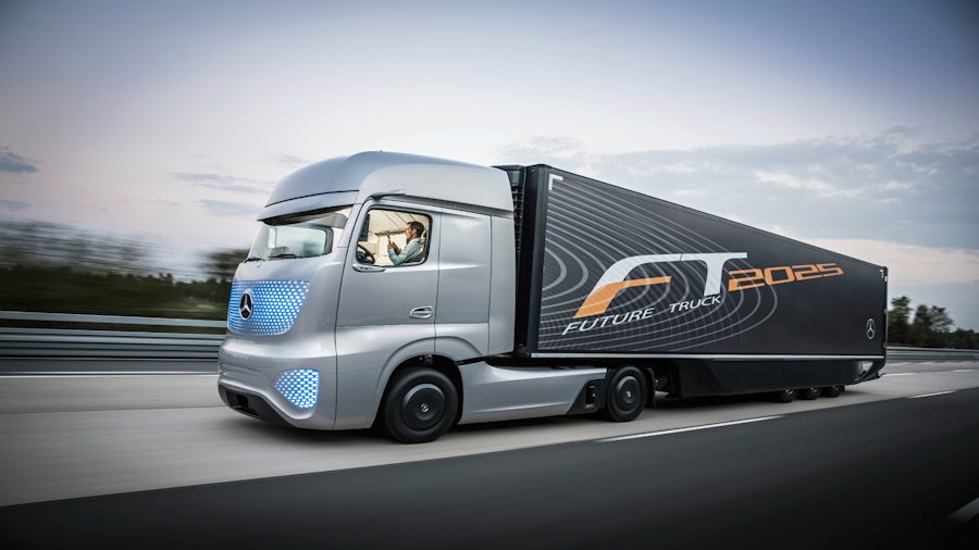 An autonomous semi truck driving from right-to-left of the camera shot. There are graphic designs on the front grill illustrating its connectivity.
