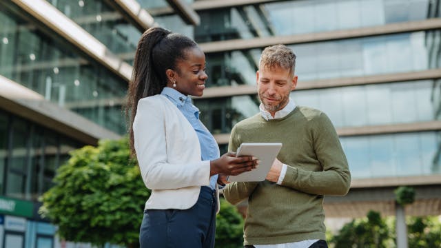 Deux collègues en train de parler devant un immeuble de bureaux, une tablette à la main.