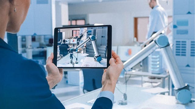 An engineer uses digital solutions on a tablet to improve the operation of a robotic arm industrial machine.