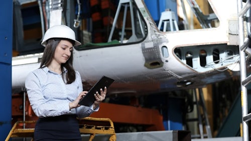 一位站在实体飞行器旁用平板查询资料的头戴安全帽的工程师，MBSE 为她连通了虚拟世界和物理世界。