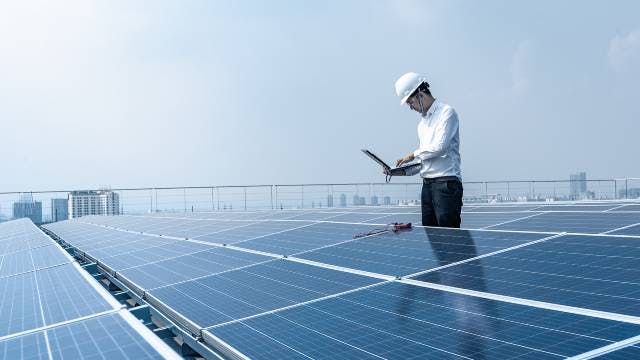 Technician working next to solar panels with laptop computer. 