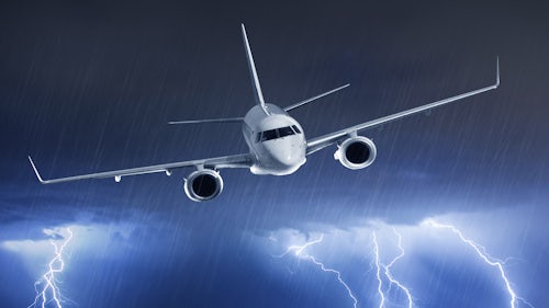 一架客机从暴雨中的乌云中飞出，一道云地闪电照亮了下方的天空。