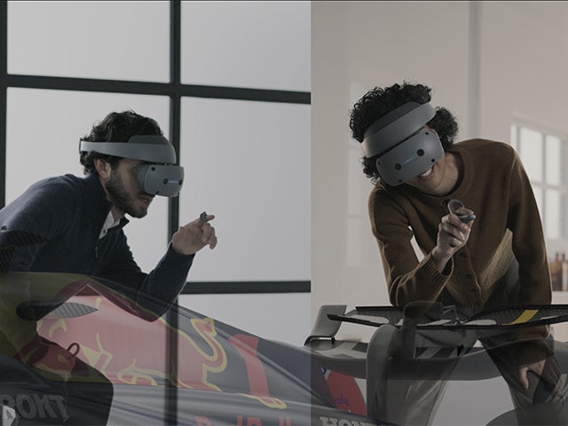 Two people wearing Sony XR head-mounted displays and controls to view an Oracle Red Bull Racing car in NX Immersive Designer