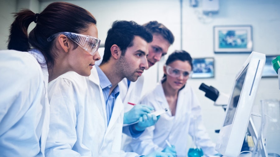 Four medical device design engineers wearing lab coats looking at a computer screen 