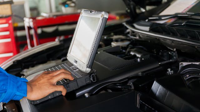 Auto mechanic using an aftermarket or aftersales diagnostics tool on an electrified vehicle in a workshop.