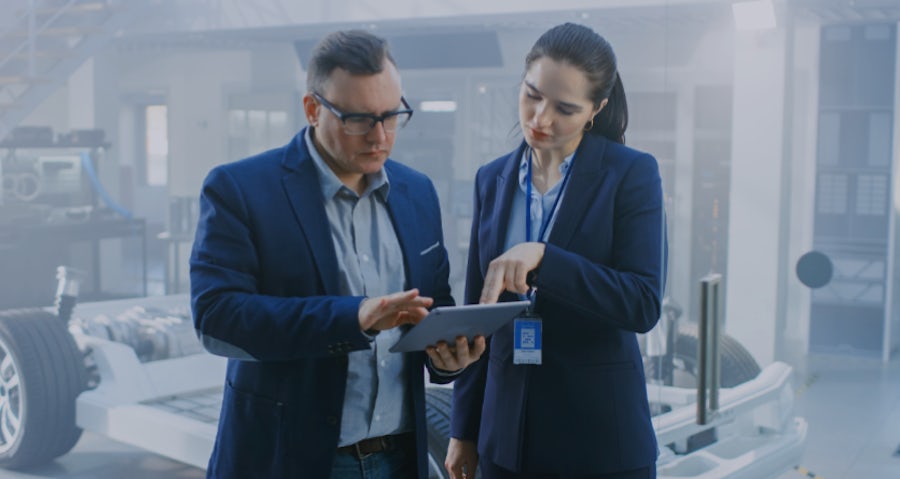 Two individuals dressed in business attire reviewing information on a tablet.