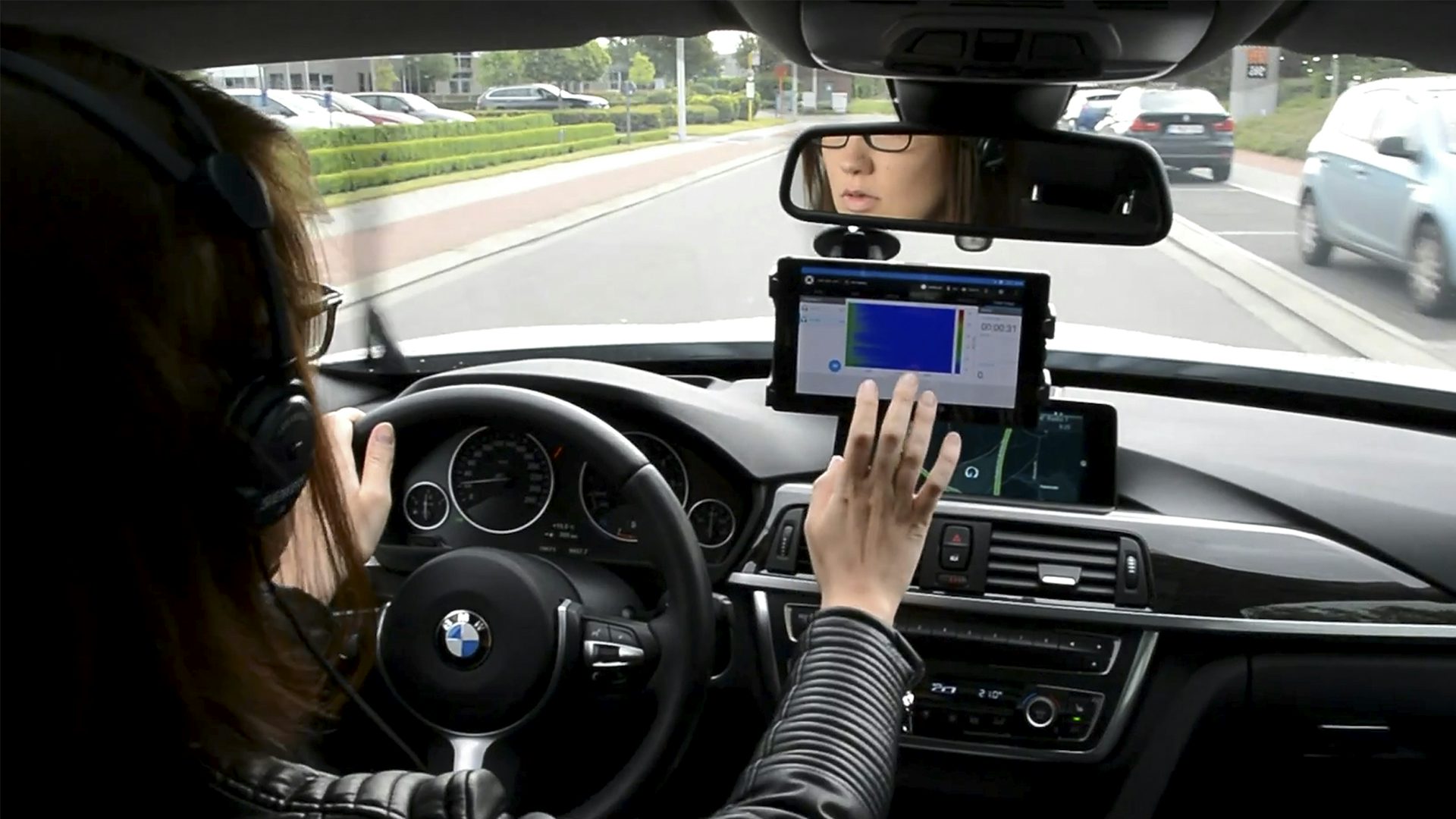 A woman driving a car while running an operational NVH testing on a device.
