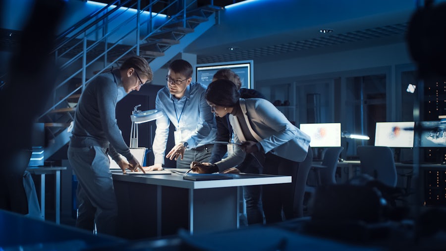 Four people huddled around a table and surrounded by computers.