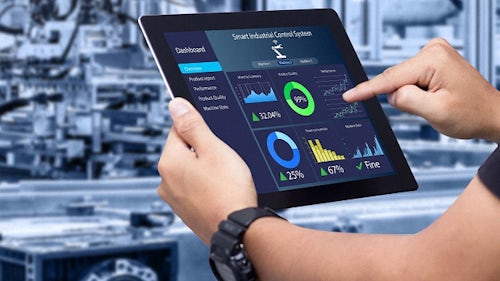 Softwarová řešení s nízkou potřebou kódu zobrazená na tabletu, který drží pracovník v dílně s průmyslovými stroji.