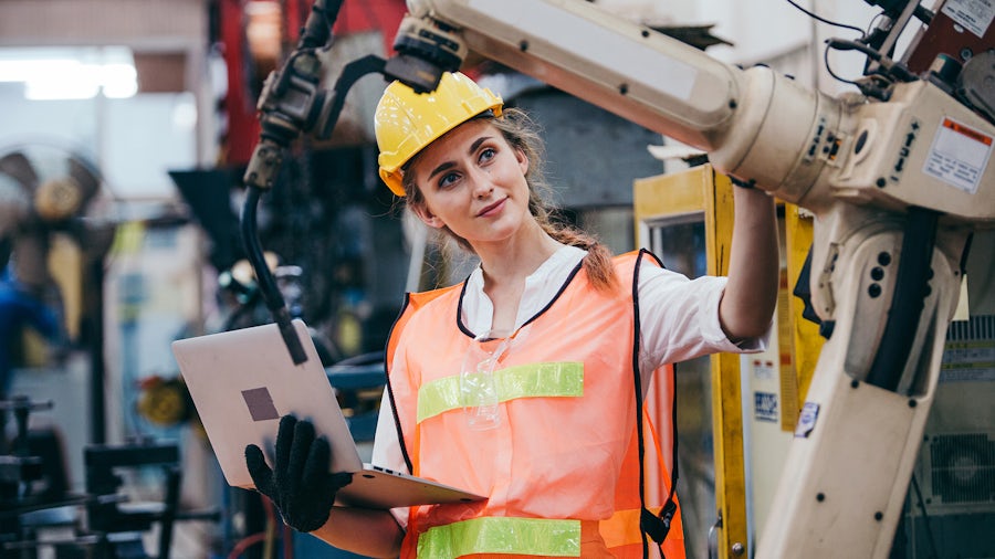 Women looking at an equipment piece in a factory line while holding a computer. 