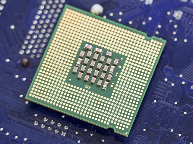 A close-up view of a computer processor chip placed on a blue printed circuit board, showcasing the intricate design and pins on the underside of the chip.