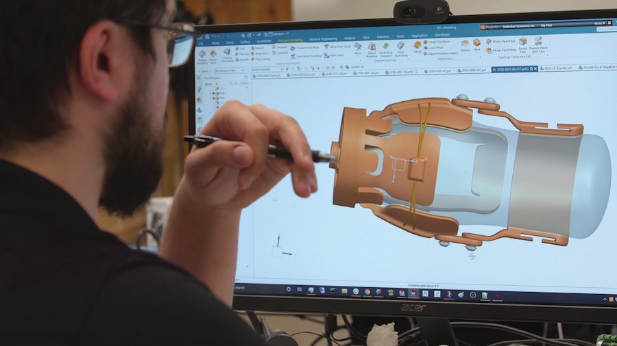 An engineer contemplates a machine component design with NX on his computer.