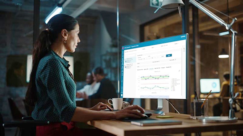 Image of a woman working on a computer in an office setting. The image represents the concept of quality inspection. 