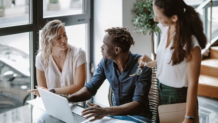Three colleagues talking around a laptop in a modern office.