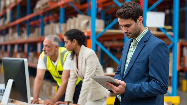 Professionals using quality management software in a warehouse setting to ensure supplier quality control and standards.