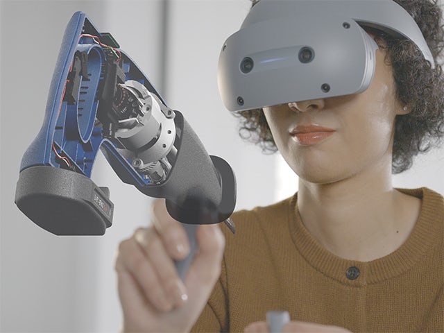 Woman wearing a Sony VR headset and using Siemens NX Immersive Designer software to manipulate a virtual model of an electric reciprocating saw.