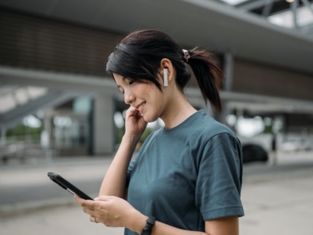 Woman looking at her phone with headphones in watching a webinar.