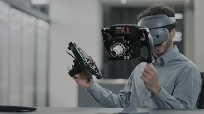 An engineer wearing a Sony XR head-mounted display while holding a real F1 steering wheel in one hand and with the other hand, 