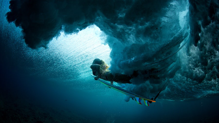 A woman underwater on a surfacing board.