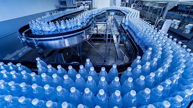 Conveyor belt in a factory holding rows on clear water bottles.