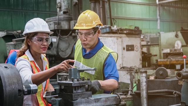 Woman and man in plant pointing to machinery