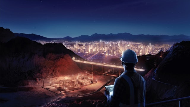 Man with hard helmet on looking over a lit-up town and city. 