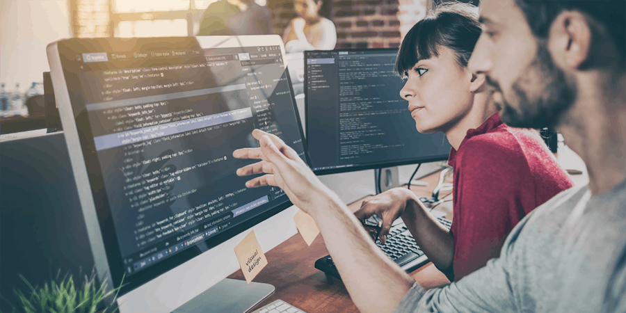 young man and young woman reading code on two monitors