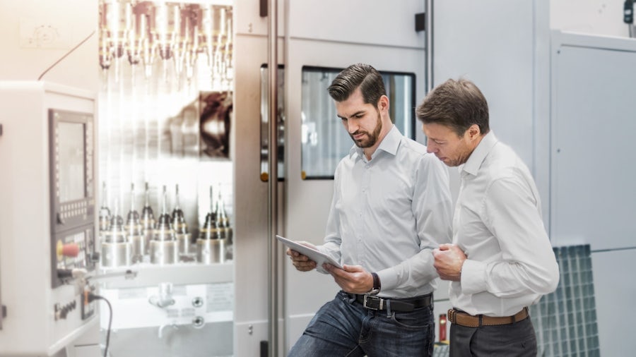 Two people look at a clipboard in front of a cnc machine 