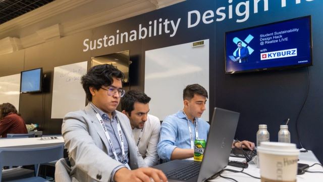 Three students sitting at a desk looking at a laptop computer working on the Sustainability Design Hack at Realize LIVE.
