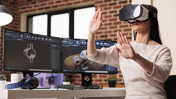 一个女人戴着 VR 头盔站在显示机器零件的电脑显示器前